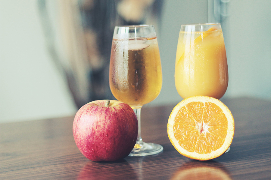 Orange juice and apple juice one a table with an apple and an orange