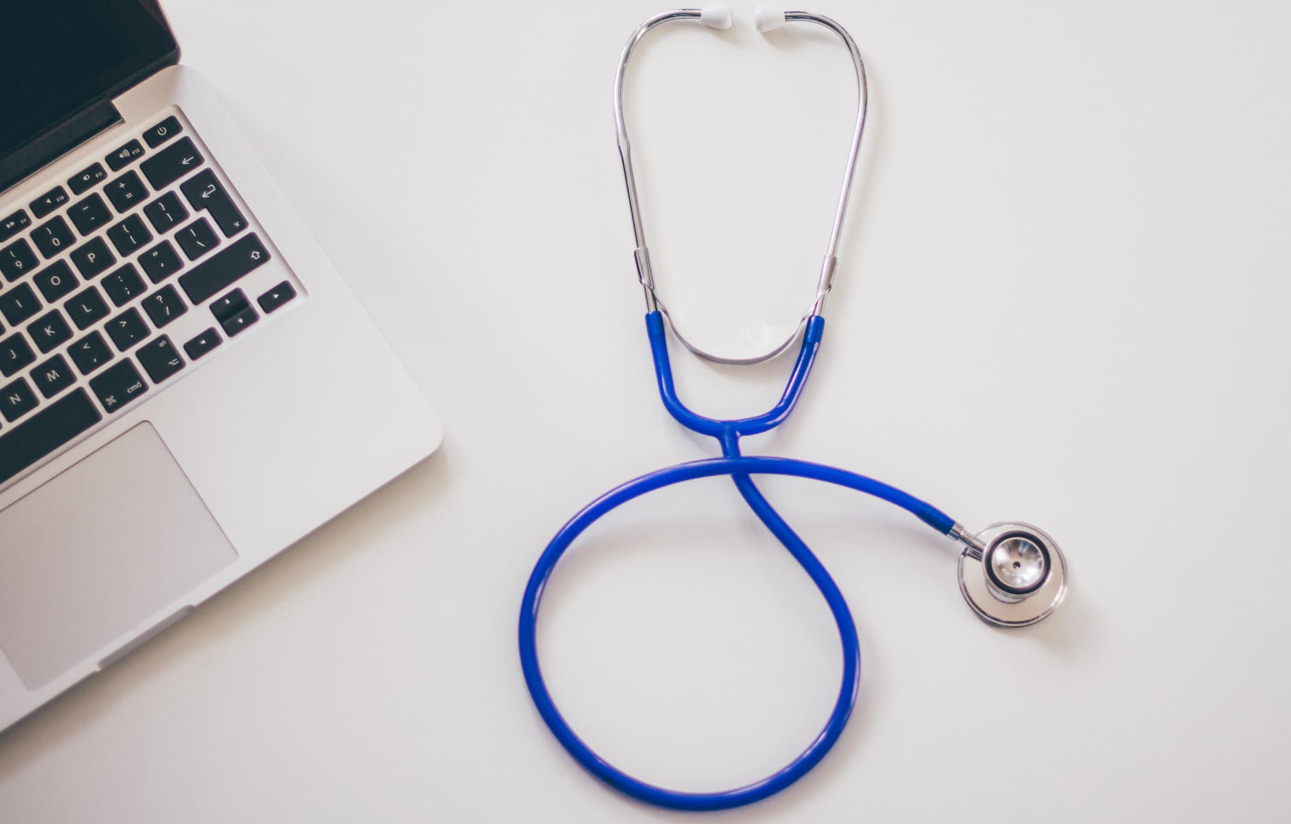 A blue stethoscope on a white table next to a laptop