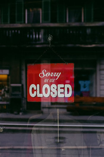 Red sign hanging from glass that says Sorry we're closed
