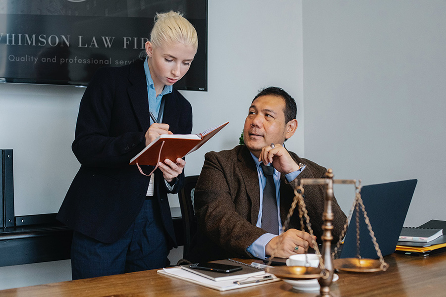 Woman writing in a book while man sits at a desk