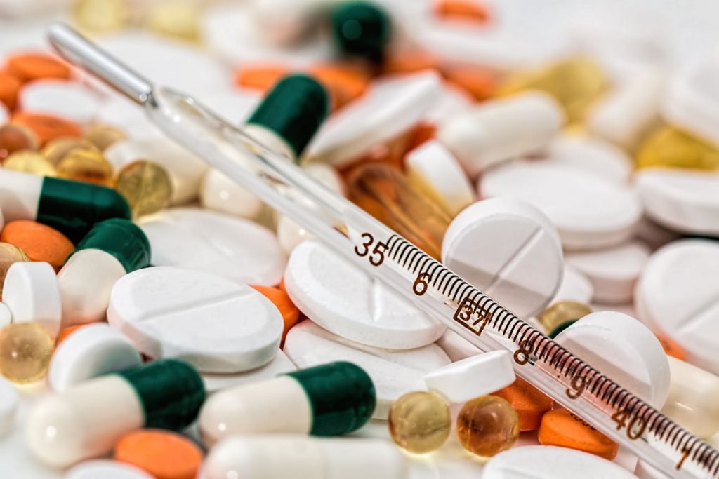 Thermometer over a pile of white orange and green pills