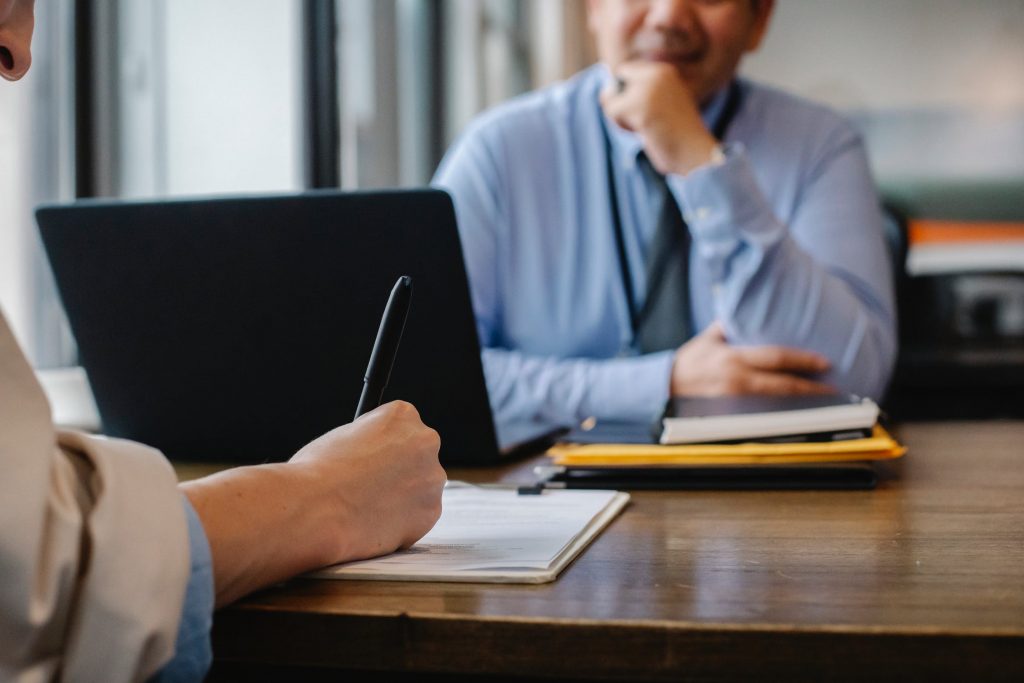 Man listening to a person behind a desk writing on a piece of paper