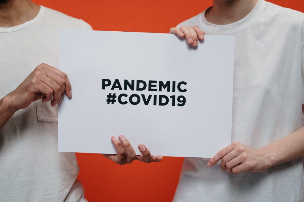 Two men in tee shirts holding a sign for the pandemic with an orange background