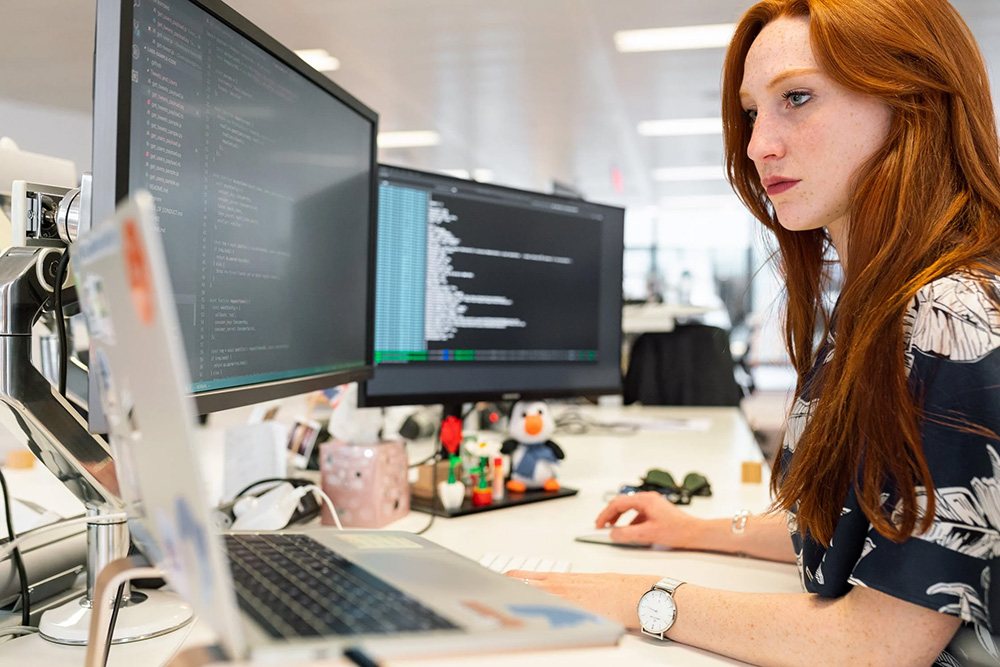 Programmer coding on double screens and a laptop