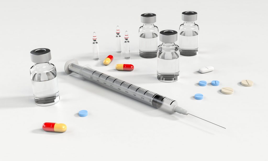 A syringe next to some pills and vials on a white table