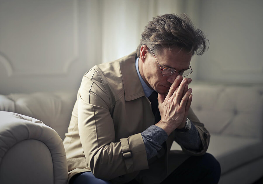 Man praying in a beige light jacket on a couch