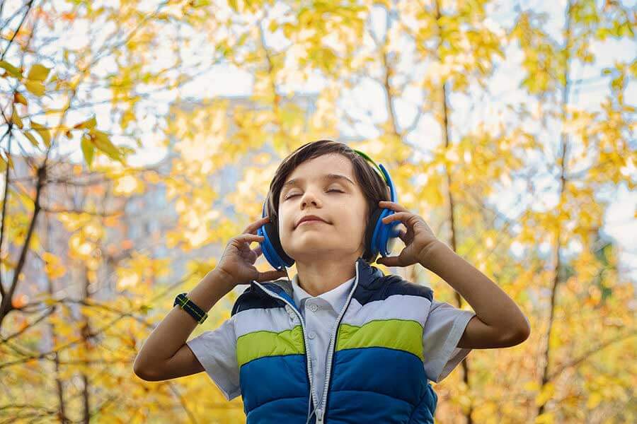 Child listening to music with blue headphones in autumn