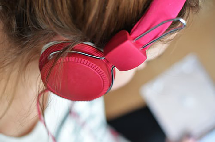 Child listening to music with pink headphones which doing homework