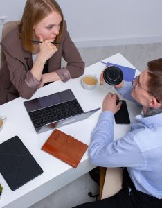 Two colleagues having a discussion over a desk with a laptop and coffee