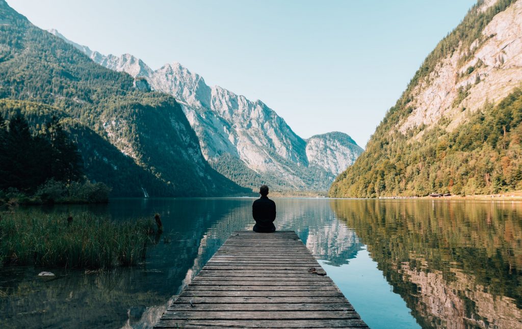 Man sitting on a lake dock viewing mountains