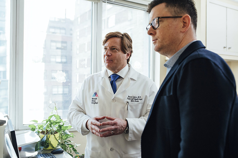 A doctor and a man in a suit having a discussion over a computer screen in an office