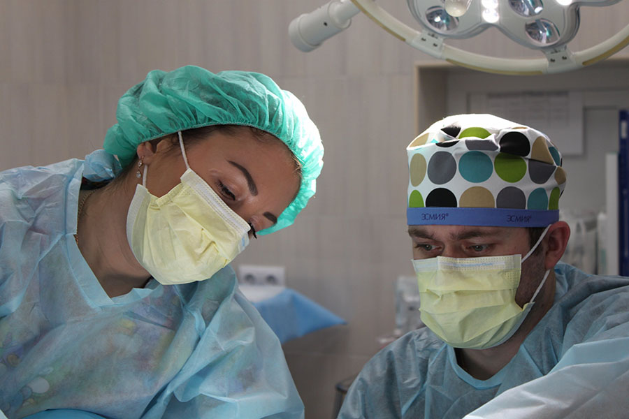 Two surgeons operating on a patient while wearing yellow face masks