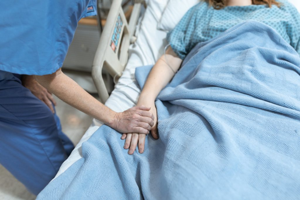 A doctor holding the hand of a patient lying in a hospital bed with a blue blanket