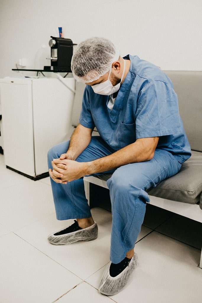 Doctor in in a face mask and scrubs praying on a couch