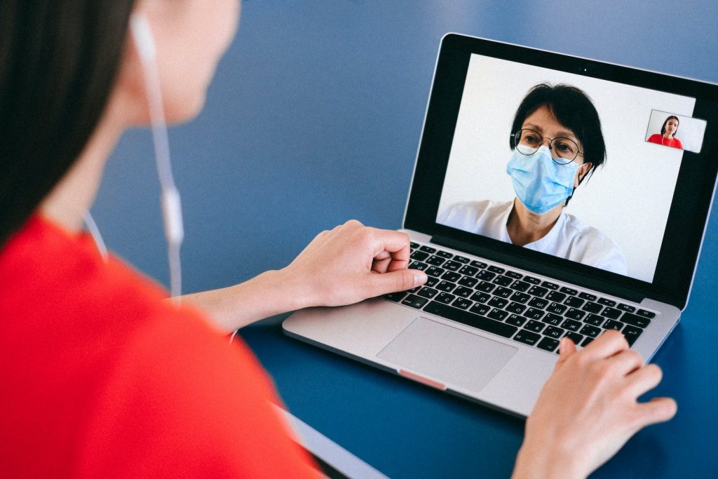 Woman in red shirt having a zoom call with a doctor on a laptop