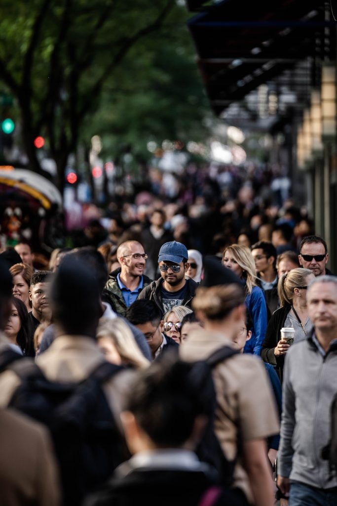 Man walking on a crowded city street with a blue hat